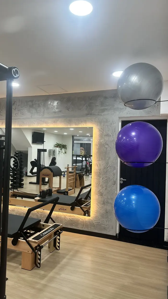 Espelho com iluminação embutida, aparelhos de Pilates e bolas suíças organizadas na parede